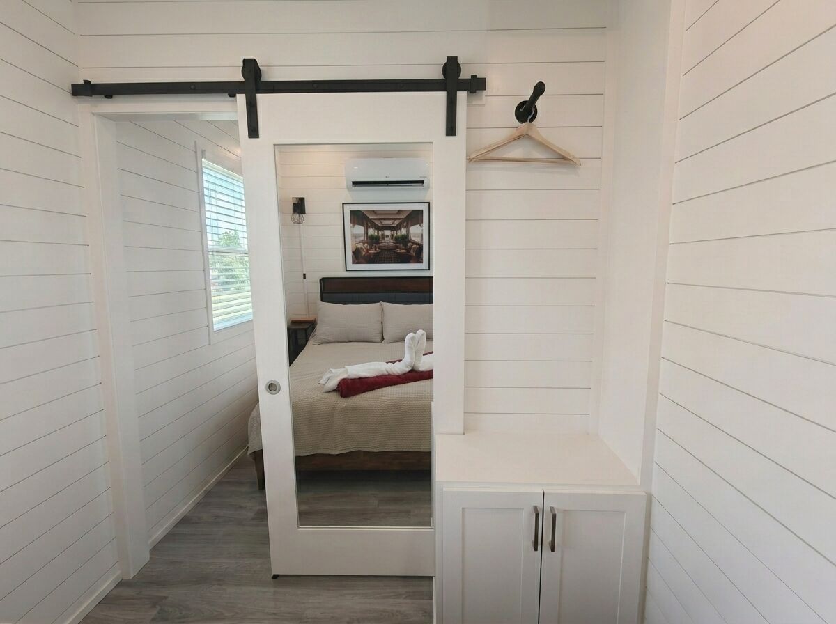 A narrow hallway with a door leading to a bedroom with a bed and a hanging light fixture.