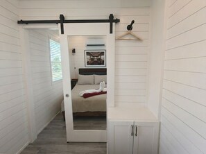 A narrow hallway with a door leading to a bedroom with a bed and a hanging light fixture. - Container Home · Rooftop Fire Pit, Pool & Wineries (Fredericksburg)