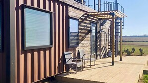 Una cabana moderna amb façana de fusta, una zona d'estar exterior coberta i una escala que condueix a un nivell superior.