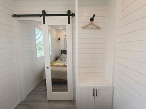 A hallway with a door leading to a bedroom, a white wardrobe, and a wooden hanger on the wall.