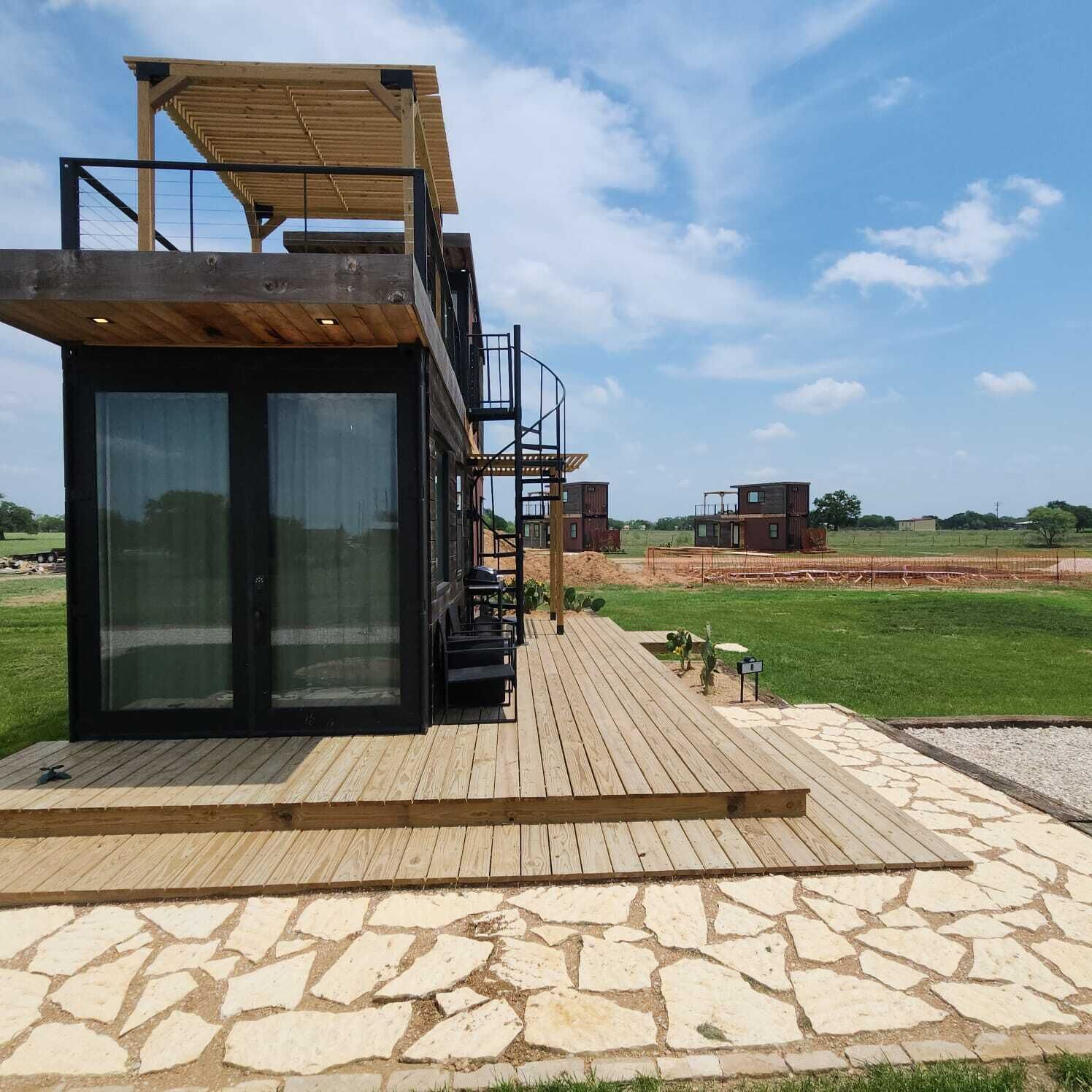 Een modern gebouw met glazen entree, houten terras en metalen trap die naar een tweede niveau leidt.