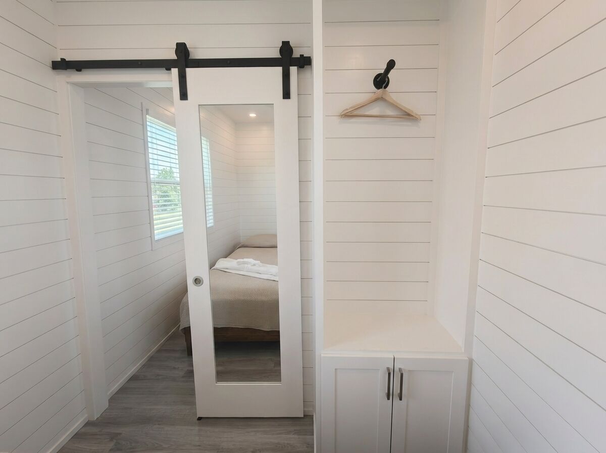 A hallway with a door leading to a bedroom, a coat rack, and a small cabinet.