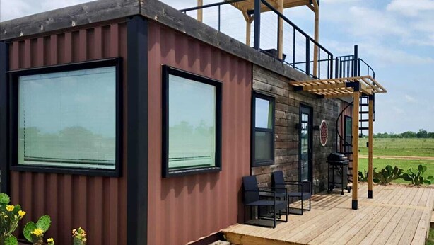 Une cabane moderne dotée de grandes fenêtres, d’une terrasse en bois et d’un espace patio.
