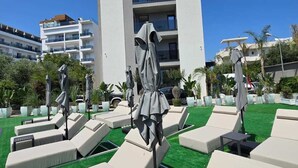 A rooftop pool area with sun loungers and umbrellas, surrounded by a white building with balconies. - Marbella Sol (Ksamil)