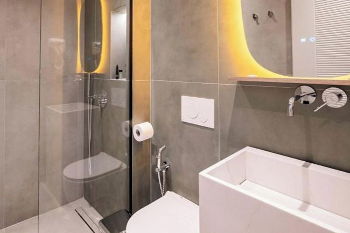 A modern bathroom with a glass-enclosed shower, a white bathtub, and a curved mirror with under-cabinet lighting.