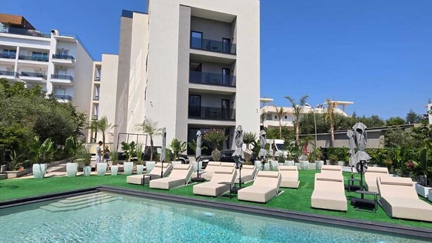 A swimming pool with lounge chairs and umbrellas, surrounded by a building with multiple floors and balconies. - Marbella Sol (Ksamil)