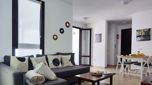 Un salon moderne avec un canapé gris, une table basse en bois et un coin repas comprenant une table et des chaises blanches.