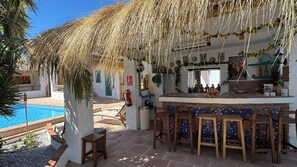 Un espace bar avec une piscine, des sièges en plein air et un toit de chaume.