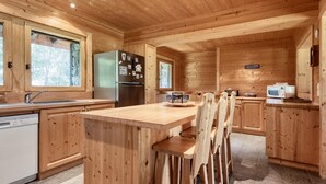A wooden cabin kitchen with a central island, wooden chairs, a refrigerator, a microwave, and a dishwasher. - Family chalet in Saint-Gervais, 6 bdr, 12 pax, WiFi, parking (Saint-Gervais-les-Bains)