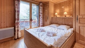 A wooden cabin bedroom with a large bed, two bedside lamps, and a sliding glass door to a balcony. - Family chalet in Saint-Gervais, 6 bdr, 12 pax, WiFi, parking (Saint-Gervais-les-Bains)