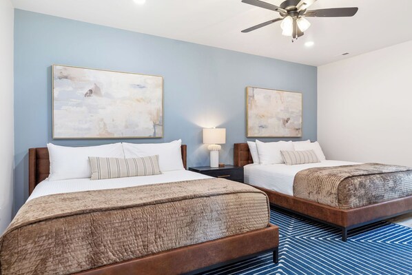 A hotel room with two beds, a ceiling fan, and artwork on the walls.