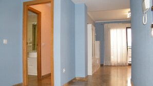 Un pasillo con una puerta de madera que da a un baño, un armario blanco y un teléfono en la pared.