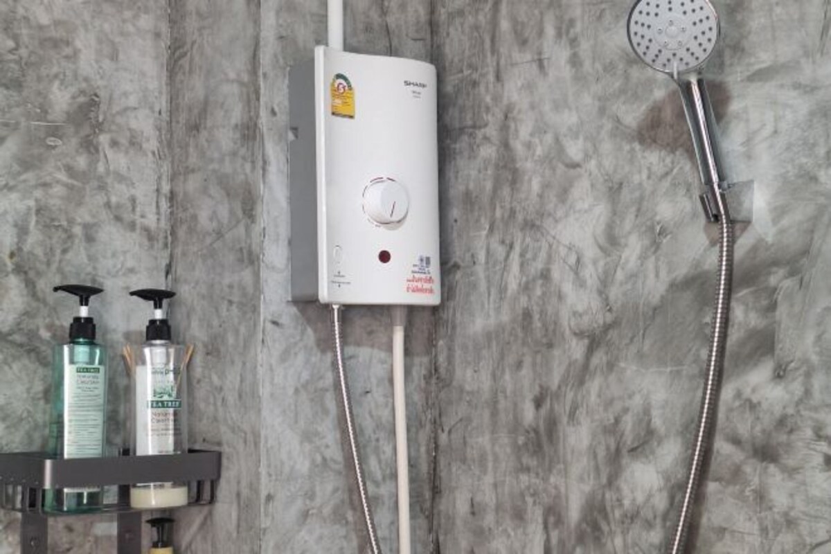 A bathroom with a white shower unit, a handheld showerhead, and two bottles of shampoo and conditioner on a shelf.