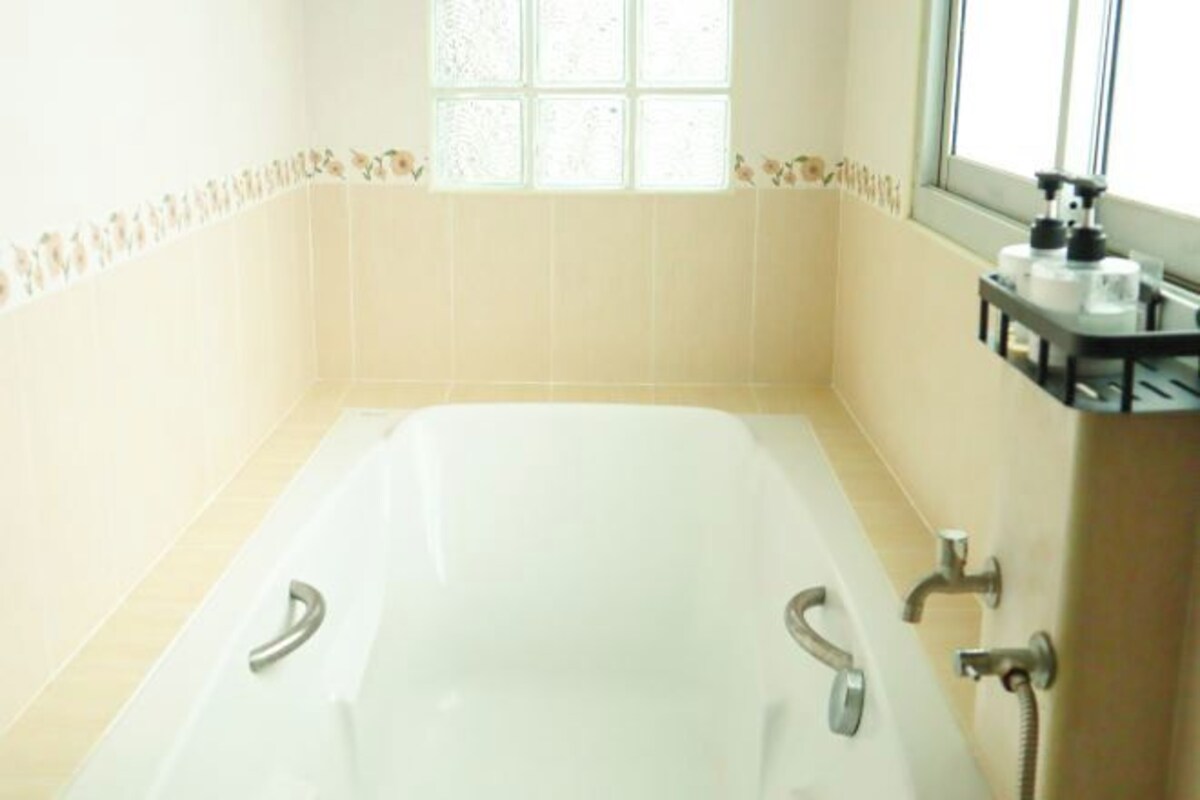 A bathroom with a bathtub, a window, and a shelf with toiletries.