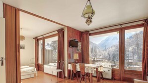 Ein Zimmer mit Holzböden, einem Esstisch mit Stühlen, einer Bank, einem Fernseher und großen Fenstern mit Blick auf die Berge.