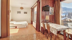 Ein Schlafzimmer mit Bett, Schreibtisch mit Stühlen, Fernseher und Blick auf eine verschneite Landschaft.