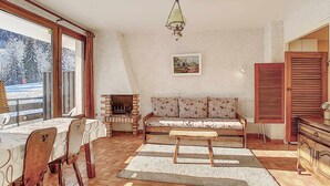 Ein gemütliches Wohnzimmer mit Kamin, einer Couch, einem Esstisch mit Stühlen und einem großen Fenster.