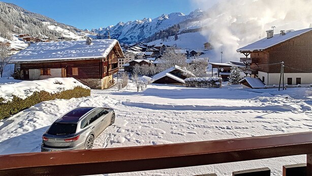 Un village de montagne enneigé, avec des bâtiments en bois, une voiture et une source de vapeur.