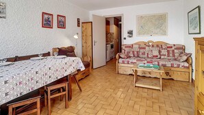 Une pièce chaleureuse avec une table à manger, un canapé et un meuble en bois. Une porte donne accès à une autre pièce.