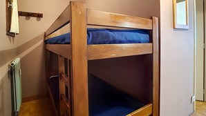 Un lit superposé avec un matelas bleu, dans une pièce aux murs de couleur claire et au plancher en bois.