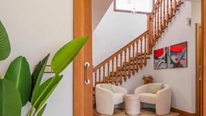 Un escalier avec des balustrades en bois menant à un palier où se trouvent deux fauteuils blancs et une petite table ronde.