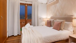 Une chambre dotée d’un grand lit, d’un plancher en bois, d’une table de chevet, d’un climatiseur mural et d’une vue sur l’extérieur, visible à travers une porte vitrée.
