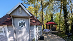 A wooden cabin with a red roof, a hexagonal window, and a door. There are two potted plants in front of the cabin.