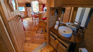 A wooden cabin interior with a kitchen, dining area, and bathroom.