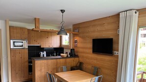 A compact kitchen with wooden cabinets, a built-in oven, a sink, and a dining area with a table and chairs.
