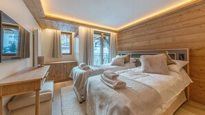 A cozy bedroom with two beds, a desk, and a window with curtains. - Luxury Apartment with Pool, Sauna and Hammam in Val-d'Isère (Val-d'Isère)