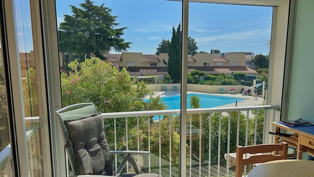A balcony with a view of a swimming pool, a chair, and a table.