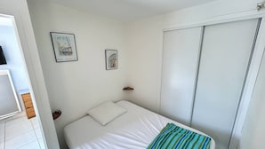 A bedroom with a bed, two framed pictures on the wall, a wooden nightstand, and a white wardrobe.