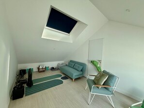 A modern loft bedroom with a skylight, a teal sofa, a green armchair, and a small side table.