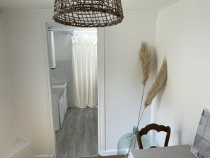 Eine Küche mit weißen Schränken, einer Netzleuchte an der Decke und Blick ins angrenzende Badezimmer.