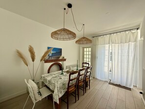 Un coin repas avec une table dressée pour quatre personnes, un luminaire suspendu et une fenêtre avec des rideaux.