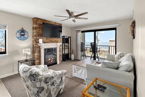 Ein Wohnzimmer mit Kamin, Deckenventilator, einer Couch, einem Couchtisch und einem Balkon mit Blick.