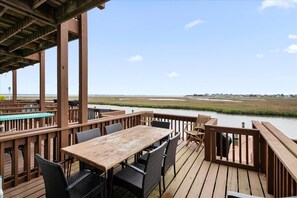 A wooden deck with outdoor furniture, a pool, and a view of a marshland.