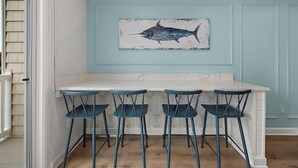 Eine Küche mit Marmorarbeitsplatte, vier blauen Barhocker und einem an der Wand hängenden Fischbild.