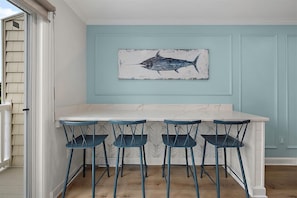 A kitchen with a marble countertop, four blue bar stools, and a wall-mounted fish painting.