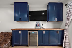 A compact kitchen with dark blue cabinets, a stainless steel dishwasher, and a flat-screen TV mounted above the counter.