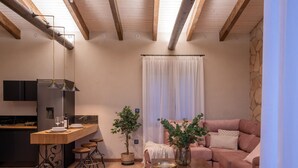 Ett modernt kök med en central köksö, en matplats med soffa och soffbord samt ett vardagsrum med ett stort fönster och gardiner.