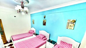 A room with two beds, each with pink patterned bedding, a white headboard, and a small table with a plant. The walls are painted blue, and there are decorative items on the wall. - Cozy apartment in tranquil Old Cairo with fitness room, WiFi (Egypt)