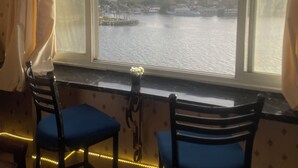 A room with a large window overlooking a river and cityscape. There are two chairs and a small table with a potted plant. - Cozy apartment in tranquil Old Cairo with fitness room, WiFi (Egypt)