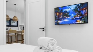 Une chambre d’hôtel avec un lit, un téléviseur diffusant des images de paysages tropicaux et une porte donnant accès à une salle de bain.