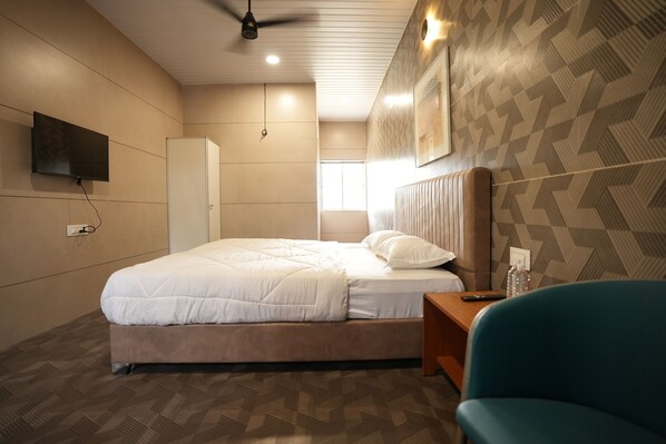 A modern hotel room with a large bed, a television mounted on the wall, a ceiling fan, and a patterned wall.
