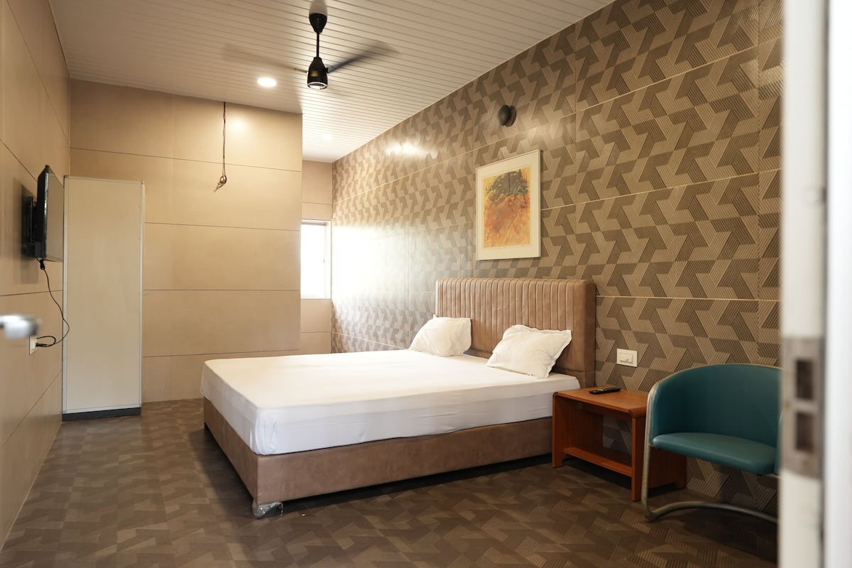 Ein modernes Hotelzimmer mit einem großen Bett, einem Schreibtisch, einem Sessel und einem Fernseher.