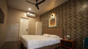 Habitación de hotel con una cama, cabecera de madera, mesita de noche, equipo de aire acondicionado, ventilador de techo y pared con diseño.