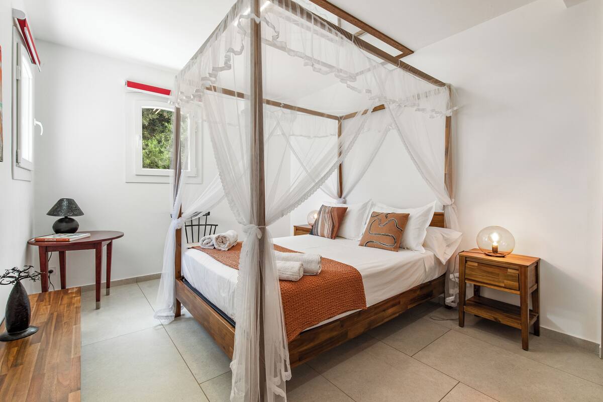 A four-poster canopy bed with a wooden frame, a bedside table with a lamp, and a nightstand with a lamp.
