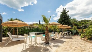 An outdoor patio with stone flooring, white lounge chairs, and thatched umbrellas. - VILLA RASOA (Agde)
