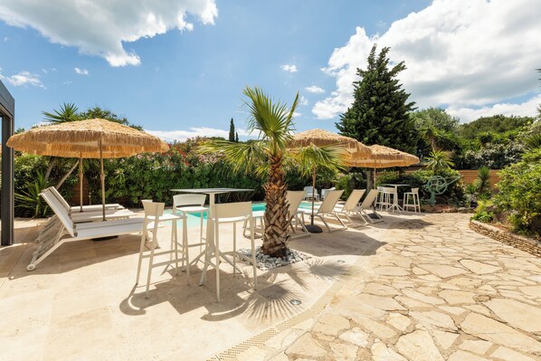 An outdoor patio with stone flooring, white lounge chairs, and thatched umbrellas. - VILLA RASOA (Agde)